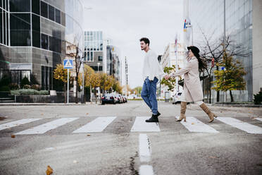 Man holding hands with woman while crossing road in city - EBBF01465