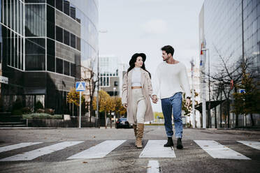 Smiling woman holding hands with male partner on road in city - EBBF01485