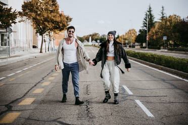 Beautiful smiling woman holding hands with male partner while standing on road in city - EBBF01508