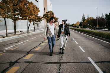 Beautiful smiling woman holding hands with partner while walking on road in city - EBBF01509