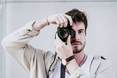 Selbstbewusster Mann, der durch die Kamera fotografiert, während er an der Wand steht - EBBF01521