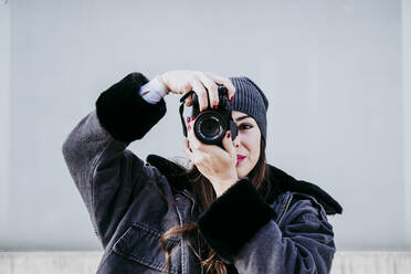 Selbstbewusste Frau, die durch die Kamera fotografiert, während sie an der Wand steht - EBBF01523