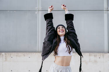 Happy female wearing jacket while standing against wall - EBBF01526