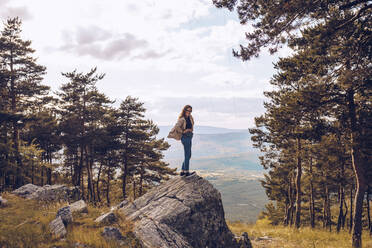 Side view of female tourist standing on rock on background of mountains and looking at camera during vacation - ADSF17362