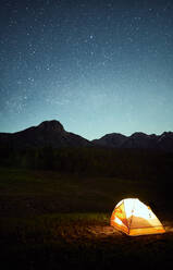 Illuminated tent placed near tree in campsite surrounded by mountains during starry night in USA - ADSF17373