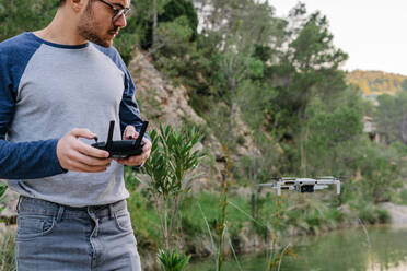 Konzentrierte männliche Steuerung moderne Drohne fliegen auf dem Hintergrund der erstaunlichen Berglandschaft und See - ADSF17375