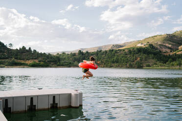 Seitenansicht von Teenager-Mädchen im Bikini und Gummiring im Moment der Sprung ins Wasser des Teiches im Sommer - ADSF17379