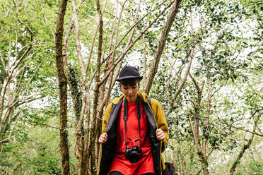 Ruhige junge Touristin in modischer Kleidung, die im grünen Wald spazieren geht und die Natur genießt - ADSF17396