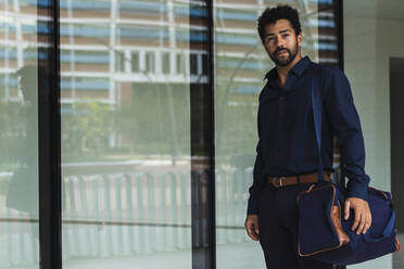 Contemplating entrepreneur with bag standing against office glass door - PNAF00076