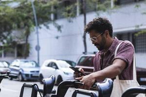 Mann benutzt Smartphone, während er auf einem gemieteten Fahrrad in der Stadt sitzt - PNAF00092