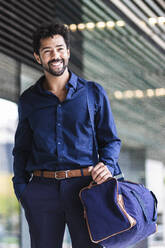 Smiling entrepreneur with bag standing in city - PNAF00106