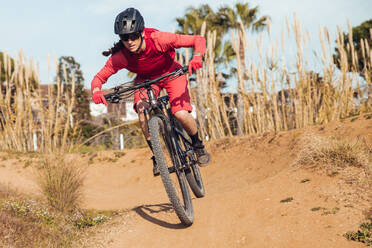 Sportlerin in schwarzem Helm und roter Sportkleidung mit Brille fährt Mountainbike auf Trainingsstrecke - ADSF17423