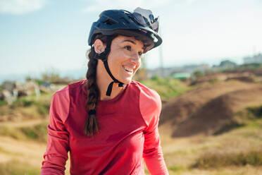 Sportlerin in schwarzem Helm und roter Sportkleidung mit Brille, die in der Nähe der Trainingsstrecke ruht und wegschaut - ADSF17424