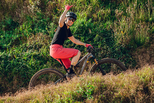 Sportlerin in schwarzem Helm und roter Sportkleidung mit Brille fährt Mountainbike auf einer Trainingsstrecke - ADSF17426