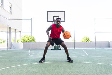 Ernster afroamerikanischer Mann, der auf einem modernen Sportplatz Basketball spielt und beim Training in die Kamera schaut - ADSF17468