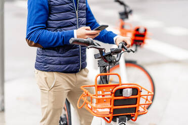 Junger Mann benutzt sein Smartphone, während er mit dem Fahrrad steht - CJMF00359