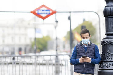 Young man using smart phone while leaning on pole in city - CJMF00361