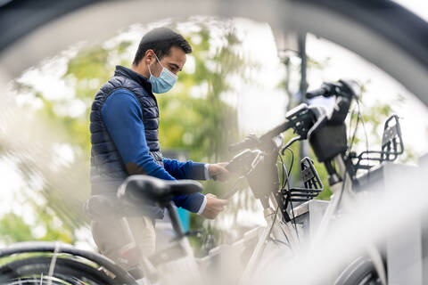 Young man using smart phone at bicycle parking station during COVID-19 stock photo