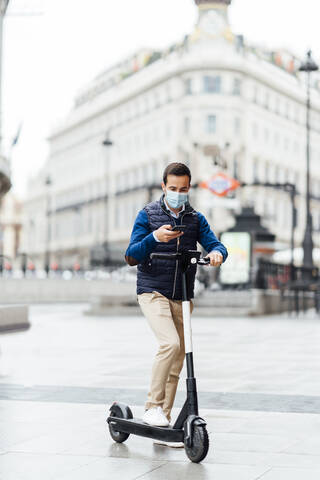 Young man doing contactless payment of electric scooter while standing on footpath during COVID-19 stock photo