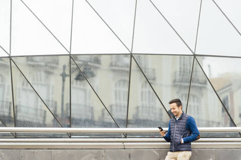 Young man using smart phone while standing against building stock photo