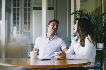 Smiling couple having coffee while sitting together at home - ABZF03439