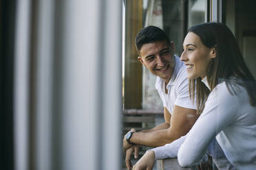 Man looking at woman while leaning on balcony railing - ABZF03446