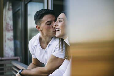 Boyfriend kissing woman while leaning at balcony railing - ABZF03447