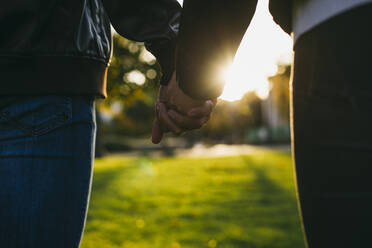 Junges Paar, das sich bei Sonnenuntergang im Freien die Hände hält - ABZF03465