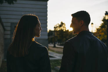 Paar, das sich bei Sonnenuntergang im Freien stehend gegenseitig ansieht - ABZF03466
