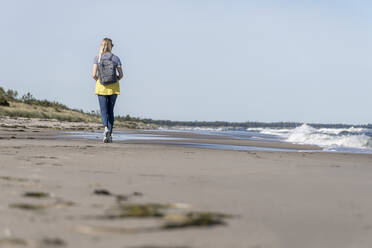 Rückansicht einer Frau mit Rucksack, die am Strand spazieren geht - CHPF00704