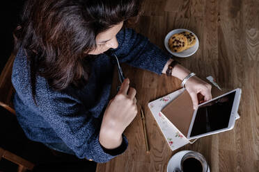 Von oben der nachdenklichen weiblichen Freiberufler sitzt am Tisch im Café und mit Tablet während der Arbeit an Startup-Projekt - ADSF17484