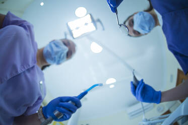 Unscharfe Zahnärztin mit Spiegel und Bohrer und Assistentin mit Absaugvorrichtung, die während der Behandlung an der Klinikdecke steht - ADSF17485