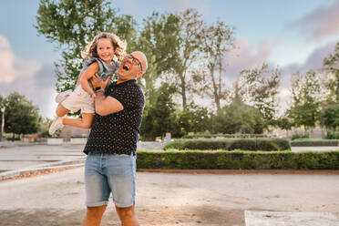 Side view of delighted father tossing daughter and standing in passage while having fun and spending weekend together in city - ADSF17544