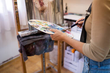 Anonymer Künstler nimmt Farbe aus einer bunten Palette, während er ein Kunstwerk im Atelier schafft - ADSF17604