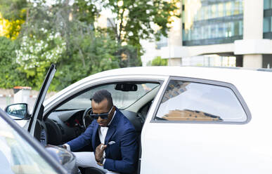Seriöser afroamerikanischer männlicher Unternehmer, der aus einem auf einer Straße in der Stadt geparkten Luxusauto aussteigt - ADSF17610