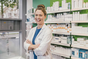 Happy pharmacist with arms crossed standing in chemist shop - MFF06800