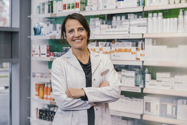 Confident female pharmacist with arms crossed in chemist shop - MFF06802