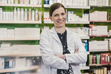 Smiling pharmacist with arms crossed in chemist shop - MFF06803