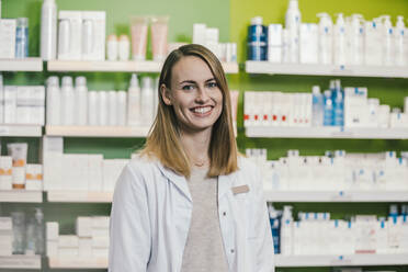 Confident pharmacist wearing lab coat while standing in chemist shop - MFF06808