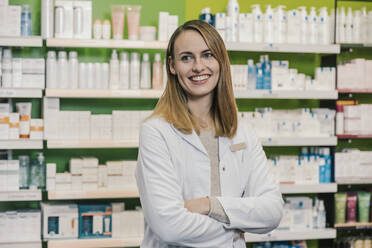 Confident pharmacist with arms crossed looking away while standing in chemist shop - MFF06809