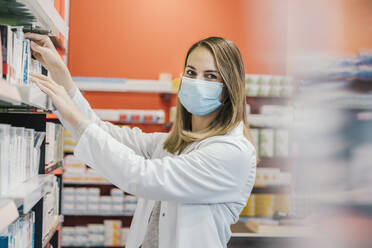 Pharmacist wearing protective face mask while working in chemist shop - MFF06811