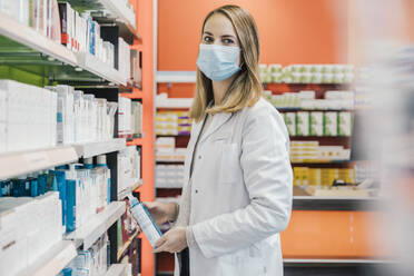 Female pharmacist wearing protective face mask while working in chemist shop - MFF06812