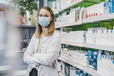 Pharmacist with arms crossed wearing protective face mask in chemist shop - MFF06814