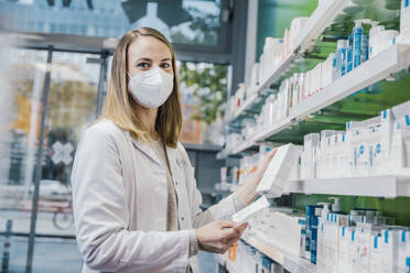Female pharmacist wearing protective face mask while working in chemist shop - MFF06817