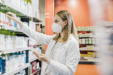 Female pharmacist wearing protective face mask while working in chemist shop - MFF06818