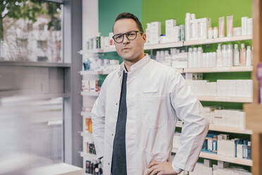 Contemplating pharmacist wearing lab coat while standing in chemist shop - MFF06820