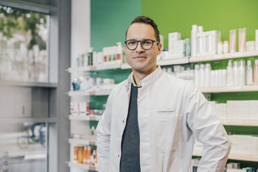 Smiling pharmacist wearing lab coat while standing in chemist shop - MFF06821