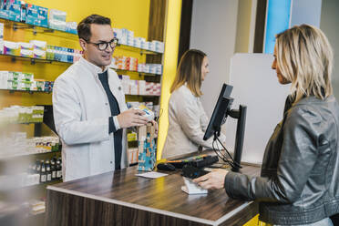 Smiling female customer giving prescription to salesman in chemist store - MFF06825