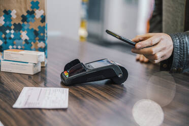 Hand of customer with smart phone at checkout counter in chemist shop - MFF06827