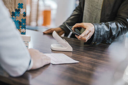 Mittelteil eines Kunden mit Mobiltelefon an der Kasse eines Drogeriemarktes - MFF06828